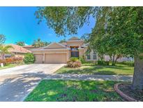 Tan single-story home featuring a well-manicured lawn and mature trees, along with a three car garage at 10212 Holland Rd, Riverview, FL 33578
