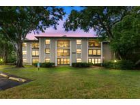 Exterior view of condo featuring large windows and balconies, surrounded by mature trees and a well-manicured lawn at 3399 Mermoor Dr # 301, Palm Harbor, FL 34685