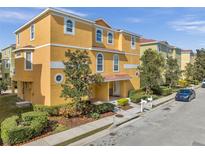 Bright yellow townhome featuring a neatly landscaped yard, decorative trees, and a well-maintained sidewalk at 456 Bayou Village Dr, Tarpon Springs, FL 34689