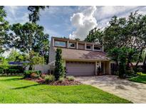 Two-story home showcasing meticulous landscaping, mature trees, and a charming, brick-paved driveway and two-car garage at 3406 Hollyhock Way, Tampa, FL 33618