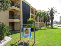 Condo exterior with lush lawn, palm trees and sign stating 