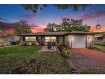Charming single-story home featuring a well-manicured lawn, inviting fountain, and cozy exterior lighting at 1179 Lazy Lake W Rd, Dunedin, FL 34698