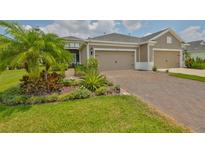 Charming home featuring a brick driveway, a 2-car garage, and beautifully landscaped front yard with tropical plants at 7406 Parkshore Dr, Apollo Beach, FL 33572