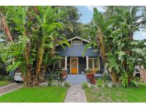 Charming two-story home featuring a blue exterior, inviting front porch, and lush tropical landscaping at 1402 E Powhatan Ave, Tampa, FL 33604