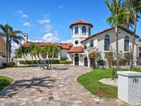 Stunning Mediterranean-style home showcasing a tower, red tile roof, circular driveway and lush landscaping at 191 1St W St, Tierra Verde, FL 33715
