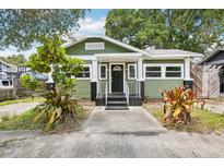 Charming green home featuring a black door, front yard plants, and a quaint front porch at 6006 N Highland Ave, Tampa, FL 33604