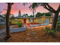 Charming yellow single-story home with a red door, well-manicured landscaping and an attached garage at 2485 Indigo Dr, Clearwater, FL 33763