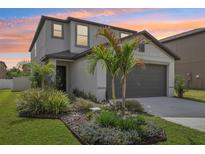 Charming two-story home with a well-manicured lawn and tropical landscaping with the sunset in the background at 6398 Bar S Bar Trl, Zephyrhills, FL 33541