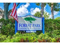 Community sign for Forest Park Condominium Association with American flag and lush landscaping at 2139 Elm St # 308, Dunedin, FL 34698
