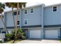 Charming multi-story townhome with a white garage door, tropical landscaping, and light blue exterior at 2643 St Josephs W Dr, Dunedin, FL 34698