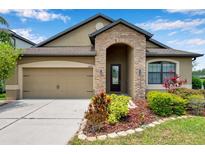 Inviting single-story home with a stone-accented entrance, well-manicured landscaping, and attached two-car garage at 11878 Thicket Wood Dr, Riverview, FL 33579