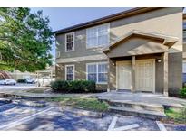 Two-story tan condo with an attached covered parking area and a well-maintained lawn and garden at 5915 Brickleberry Ln # 103, Zephyrhills, FL 33541