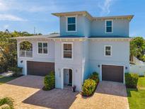 Two-story light blue home boasting a paver driveway, two-car garage, and a balcony at 7115 Bay St, St Pete Beach, FL 33706