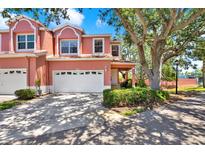 Charming pink townhouse featuring a two-car garage and lush landscaping at 14561 El Paseo Dr, Seminole, FL 33776