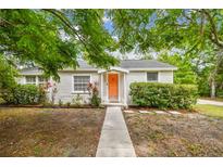 Charming single-story home featuring a neatly landscaped yard, a bright coral-colored front door, and mature shade trees at 670 Wooddell Dr, Safety Harbor, FL 34695