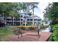Scenic view of a multi-story condo building overlooking a tranquil canal with lush landscaping and a relaxing dockside bench at 2533 Dolly Bay Dr # 203, Palm Harbor, FL 34684