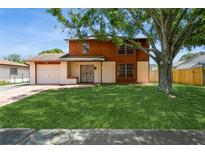 Charming two-story home featuring wood and white accents, a lush green lawn, and a mature shade tree in the front yard at 7317 W Pocahontas Ave, Tampa, FL 33634