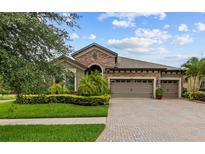 Charming home featuring a three-car garage, manicured lawn, and stone facade, and a brick-paved driveway at 1002 Cavour Ct, Brandon, FL 33511