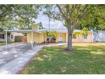 Charming yellow home featuring a welcoming front yard, palm trees, and covered carport at 1713 W Louisiana Ave, Tampa, FL 33603