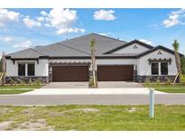 New construction townhome with a gray roof, two-car garage, and stone facade at 35571 Stableton Ln, Zephyrhills, FL 33541