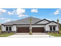 New construction duplex featuring wood garage doors, stone accents, and a tile roof under a bright sky at 35571 Stableton Ln, Zephyrhills, FL 33541