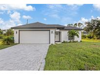 Charming one-story home featuring a white exterior, well-manicured lawn, and a paved driveway leading to an attached garage at 12106 Clarendon Ave, Port Charlotte, FL 33981