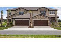 Modern townhome exterior with stone accents, dark garage doors, and well-maintained landscaping at 35609 Stableton Lane, Zephyrhills, FL 33541