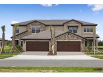 New townhome exterior featuring stone accents, a tile roof, and individual driveways leading to spacious two-car garages at 35617 Stableton Lane, Zephyrhills, FL 33541