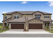 A beautiful townhouse featuring a stone facade and two-car garage with brick paver driveway at 35617 Stableton Lane, Zephyrhills, FL 33541