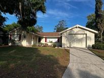 Charming single-story home with an attached garage, a well-manicured lawn, and mature trees at 12415 Stagecoach Ln, Hudson, FL 34667