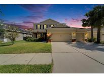 Two-story tan home with a three-car garage, manicured lawn, and palm trees at 17510 Bright Wheat Dr, Lithia, FL 33547