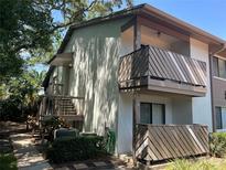 Two-story condo with wooden balcony and stairs framed by trees and lush greenery at 647 Fairmont Ave # C, Safety Harbor, FL 34695