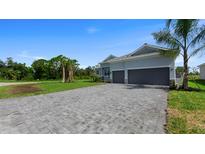 A beautiful single-story home with a large paver driveway, grey stucco, a 2-car garage, and tropical landscaping at 9295 Rosebud Cir, Port Charlotte, FL 33981