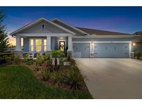 Charming single-story home with a three-car garage, inviting front porch, and beautifully landscaped yard at dusk at 8916 Windlass Cv, Parrish, FL 34219