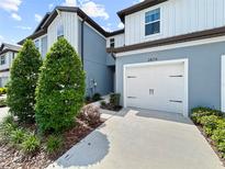 Two-story townhome features a white garage door, blue siding, and manicured landscaping at 2874 Deer Pine Trl, Land O Lakes, FL 34638