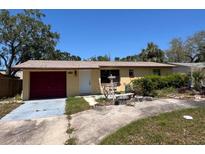Charming single-story home with mature trees, a red garage door, and a well-lit entrance at 12049 132Nd Ave, Seminole, FL 33778