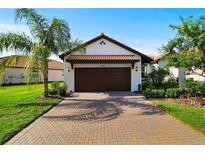 Charming home featuring a tile roof, brick driveway, and lush landscaping, creating great curb appeal at 16913 Anchor Root St, Wimauma, FL 33598