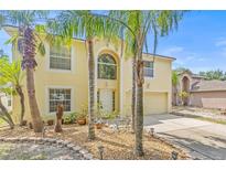 Charming two-story home featuring a two car garage, light yellow paint and mature landscaping and palm trees at 10311 Frog Pond Dr, Riverview, FL 33569