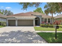 Lovely home showcasing well-manicured landscaping, a three-car garage, and a gray stucco exterior at 15711 Starling Dale Ln, Lithia, FL 33547