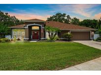 Charming single-story home featuring a manicured lawn and a welcoming front entrance with red door and arched portico at 3041 Colonial Ridge Dr, Brandon, FL 33511