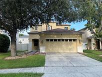 Two-story home featuring an attached two car garage, tan paint, lush tree cover, and landscaped flower beds at 9126 Lantern Oak Way, Land O Lakes, FL 34638