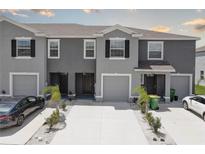 A row of gray townhomes with driveways and minimalistic landscaping featuring palm trees, small bushes, and white gravel at 33062 Frosted Clover Way, Wesley Chapel, FL 33545