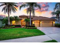 Inviting home exterior with lush landscaping, terra cotta roof, and a three-car garage as the sun sets at 984 Chickadee Dr, Venice, FL 34285
