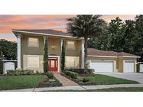 Charming two-story home featuring a red door, lush landscaping, and a three-car garage at 11029 Lynn Lake Cir, Tampa, FL 33625