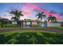 Charming home featuring mature palm trees, a circular driveway, and a well-maintained lawn under a beautiful sunset sky at 4191 Maple Ne St, St Petersburg, FL 33703