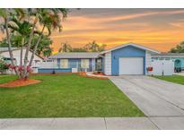 Charming blue single-story home with a well-manicured lawn, palm trees, and a freshly painted garage door at 6471 109Th N Ter, Pinellas Park, FL 33782