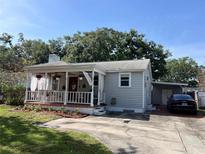 Charming home featuring a covered front porch, red door, gray siding, and mature landscaping at 1003 W Indiana Ave, Tampa, FL 33603