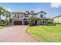Elegant two-story home featuring a brick driveway, manicured lawn, and a charming balcony at 17724 Daisy Farm Dr, Lutz, FL 33559