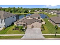 Beautiful home featuring a manicured lawn, stone accents, a three-car garage and a picturesque lake view at 18428 Malinche Loop, Spring Hill, FL 34610