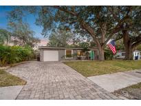 Charming home with a well-manicured lawn, brick driveway, mature trees, and an American flag at 4324 S Clark Ave, Tampa, FL 33611